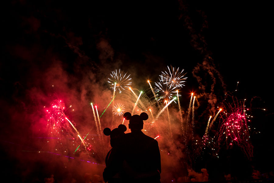 Silhouettes wearing Mickey ears watching colorful fireworks